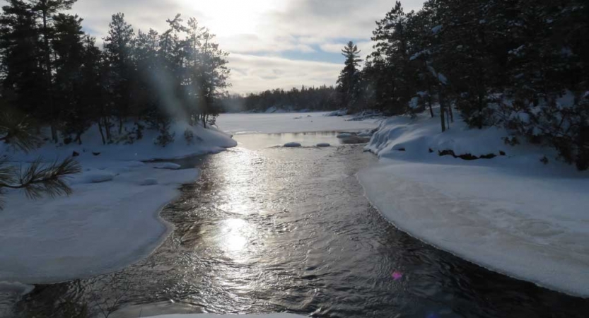 a river flows through a snowy landscape withe trees lining the shore.